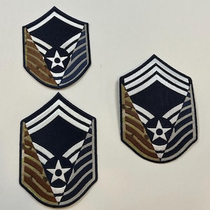 May include: Three embroidered patches featuring a dark blue shield shape with a white star and stripes. The patches have brown, silver, and blue accents, and are likely military insignia.