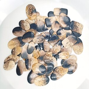 May include: A collection of natural stone cabochons in various shapes and sizes. The stones are a mix of brown and black with swirling patterns.