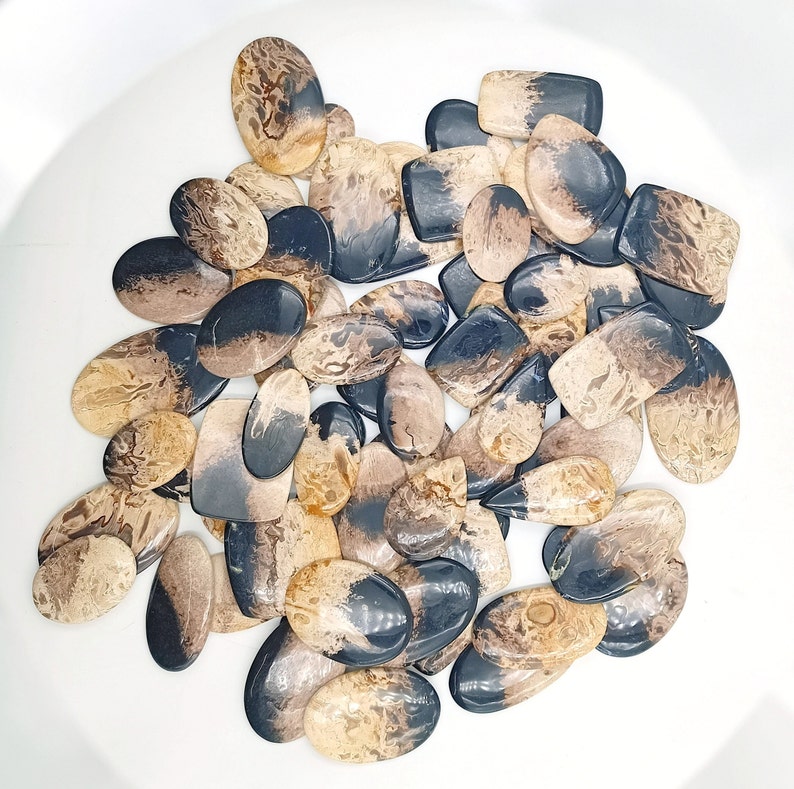 May include: A collection of natural stone cabochons in various shapes and sizes. The stones are a mix of brown and black with swirling patterns.