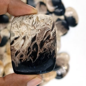 May include: A black and white agate cabochon with a swirling pattern. The cabochon is rectangular and has a smooth, polished surface.