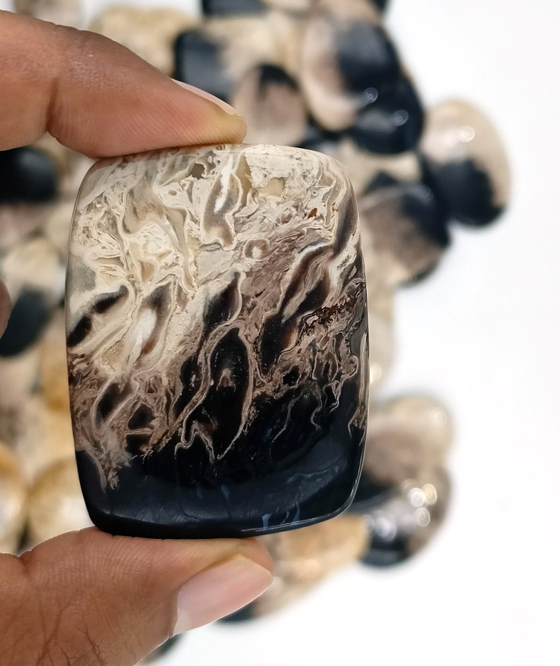 May include: A black and white agate cabochon with a swirling pattern. The cabochon is rectangular and has a smooth, polished surface.