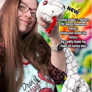 May include: A woman holds a white crocheted snake toy with black accents. The snake is 44 inches long and is a big, cuddly snake toy. The text on the image reads "Crochet Snake Pattern PDF Digital Download Pattern Amigurumi Snake Toy Pattern Big Cuddly Snake Toy Yields 44 inches long".