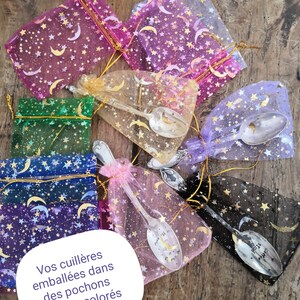 Pu&ograve; includere: Assortimento di cucchiai decorativi in sacchetti di organza colorati. I sacchetti sono adornati con stelle dorate e lune crescenti. I cucchiai presentano disegni decorativi e testo. I sacchetti sono in vari colori, tra cui rosa, verde e viola.