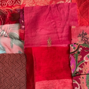 May include: A patchwork of fabric scraps in various shades of red and pink. The fabric pieces are sewn together to create a quilt-like design. Some of the fabric pieces have intricate patterns, while others are plain.