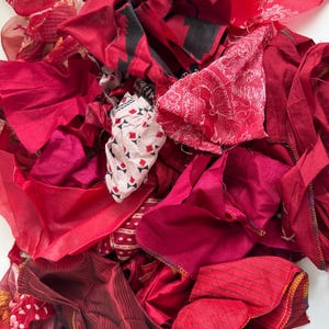May include: A pile of red fabric scraps in various shades and textures, including striped, patterned, and plain fabrics.