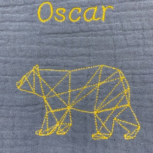 May include: A gray fabric baby blanket with the name "Oscar" embroidered in yellow thread. A geometric bear design is also embroidered in yellow thread.