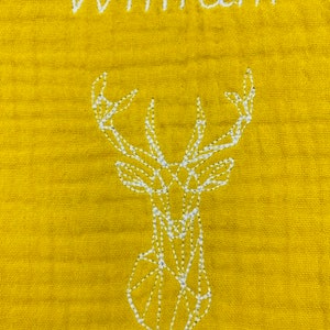 May include: A yellow baby blanket with white embroidery of a geometric deer and the name "William".
