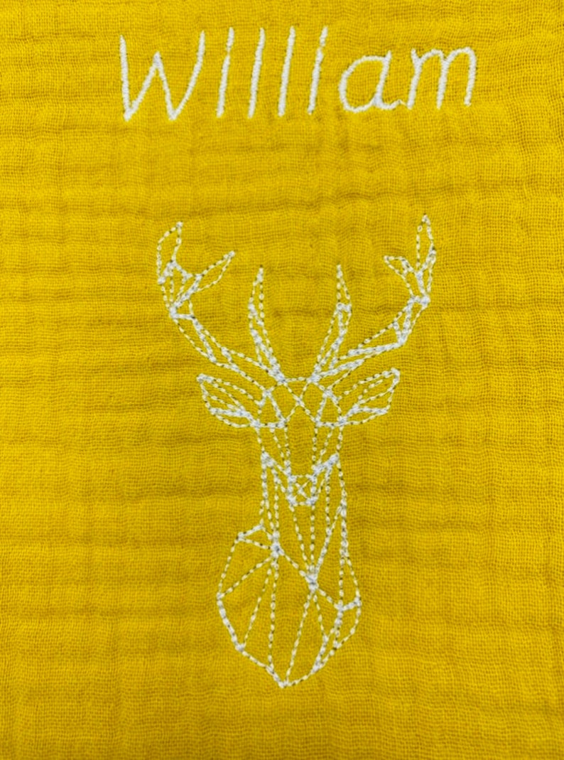 May include: A yellow baby blanket with white embroidery of a geometric deer and the name "William".