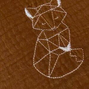 May include: A brown fabric baby blanket with white embroidery of a geometric fox and the word "Nino".