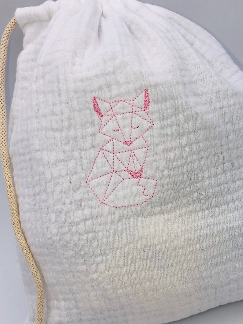 May include: White drawstring bag with a pink geometric fox design embroidered on the front.