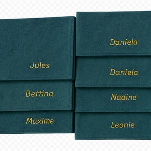 Op de afbeelding: Teal stoffen organizers met goud geborduurde namen: Jules, Bettina, Maxime, Daniela, Nadine en Leonie. Elke organizer heeft een flap. De organizers zijn in twee kolommen gestapeld.