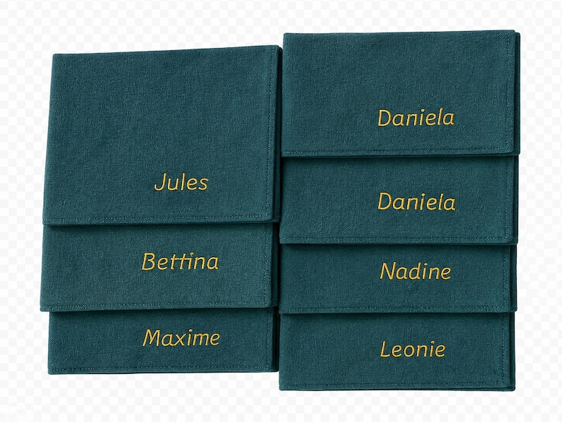 Op de afbeelding: Teal stoffen organizers met goud geborduurde namen: Jules, Bettina, Maxime, Daniela, Nadine en Leonie. Elke organizer heeft een flap. De organizers zijn in twee kolommen gestapeld.