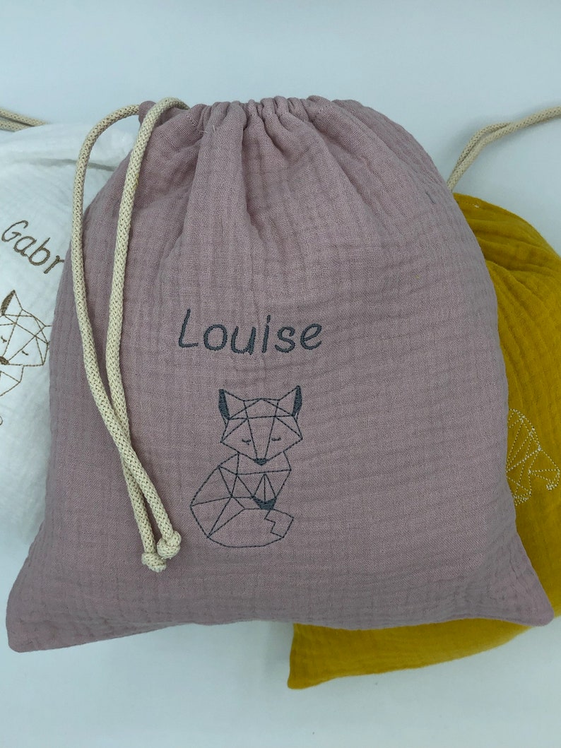 May include: A dusty rose drawstring bag with a geometric fox design and the name "Louise" embroidered on the front.
