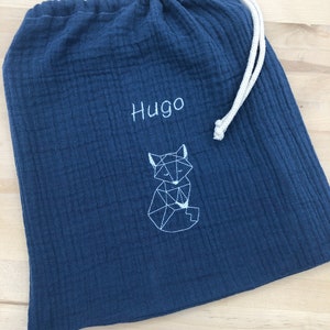 May include: A dark blue fabric drawstring bag with a white geometric fox design and the name "Hugo" embroidered on the front.
