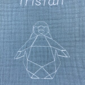 May include: A light blue baby blanket with the name "Tristan" embroidered in white. A white geometric penguin is also embroidered on the blanket.