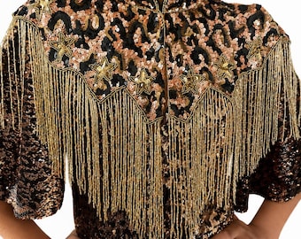 May include: A high-neck top covered in black and bronze leopard print sequins. The garment features a pointed yoke adorned with gold star-shaped appliqués and long, dangling gold fringe that extends across the chest and shoulders.