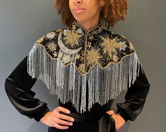 May include: A black velvet jumpsuit with a gold and silver beaded fringe collar. The collar features a crescent moon and star design.
