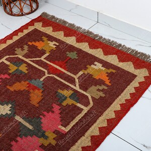 May include: A red, brown, and beige area rug with a geometric pattern. The rug has a fringe border.