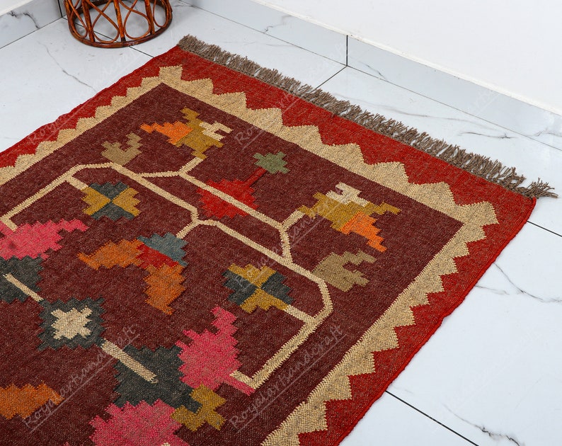 May include: A red, brown, and beige area rug with a geometric pattern. The rug has a fringe border.