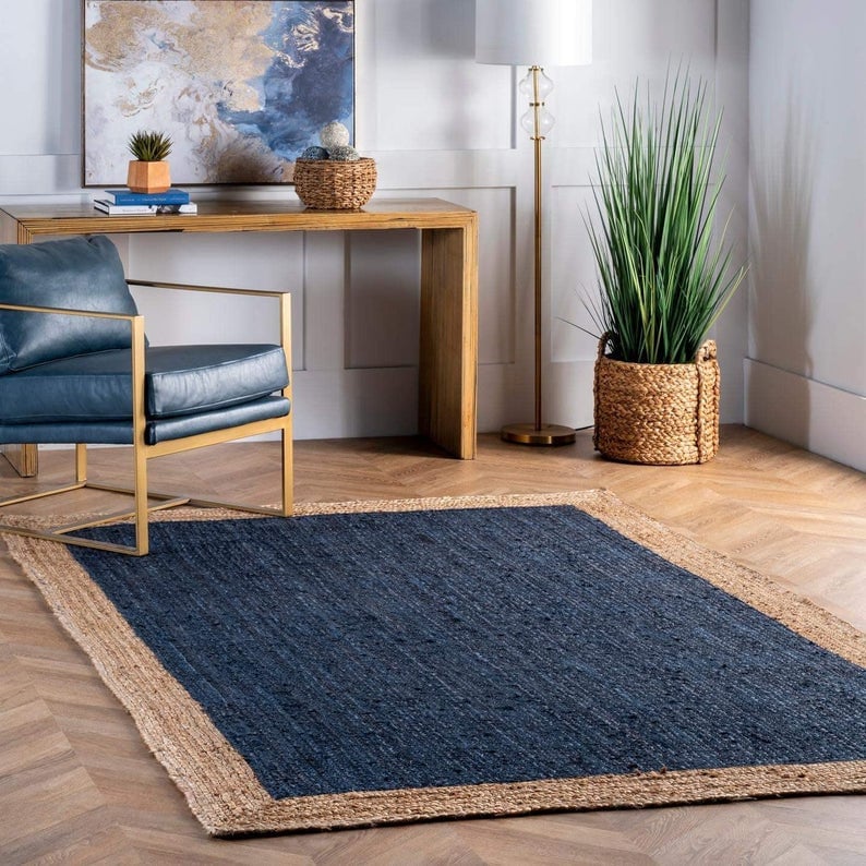 May include: A blue and natural jute rug with a thick, woven border. The rug is laid out on a hardwood floor in a living room setting.