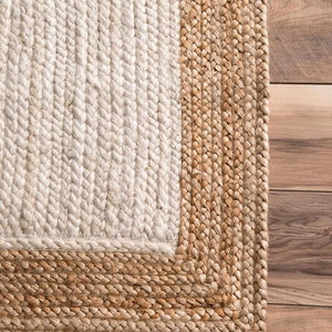 May include: A natural fiber rug with a white center and a brown border. The rug is made of woven jute and has a textured surface.