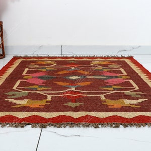May include: A red, brown, and beige area rug with a geometric pattern. The rug has a fringe border.