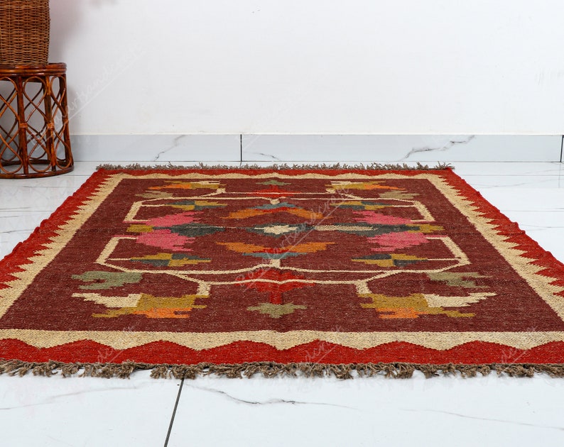 May include: A red, brown, and beige area rug with a geometric pattern. The rug has a fringe border.