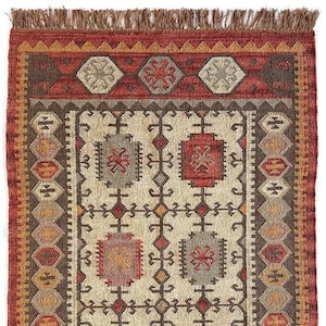 May include: Close-up of a rectangular rug with a detailed geometric pattern. The rug features a cream-coloured central field with repeating motifs in red, brown, grey, and yellow. A red border with a fringe edge frames the design, showcasing a traditional style.
