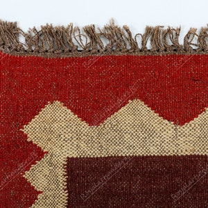 May include: Close-up of a red, brown, and beige woven rug with a geometric pattern. The rug has a fringe border.