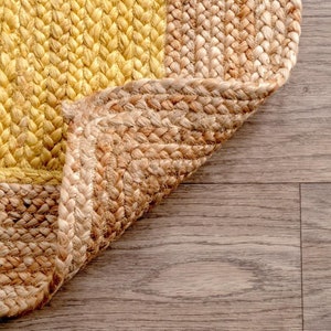 May include: A close-up of a woven jute rug with a yellow and natural brown color scheme. The rug is folded over on itself, revealing the woven texture.