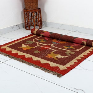 May include: A red, brown, and beige handwoven rug with a geometric pattern. The rug has a fringe border and is rolled up on a white tiled floor.