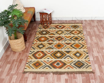 May include: A beige, brown and orange geometric patterned rug with fringe on the edges. The rug is laid out on a wooden floor.