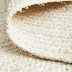 May include: Close-up of a white woven rug with a textured surface. The rug is made of natural fibers and has a simple, elegant design.