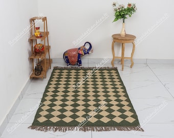 May include: A green and beige diamond patterned rug with fringe edges. The rug is on a white tiled floor.