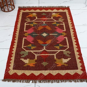May include: A red, brown, and beige area rug with a geometric pattern. The rug has a fringe border.