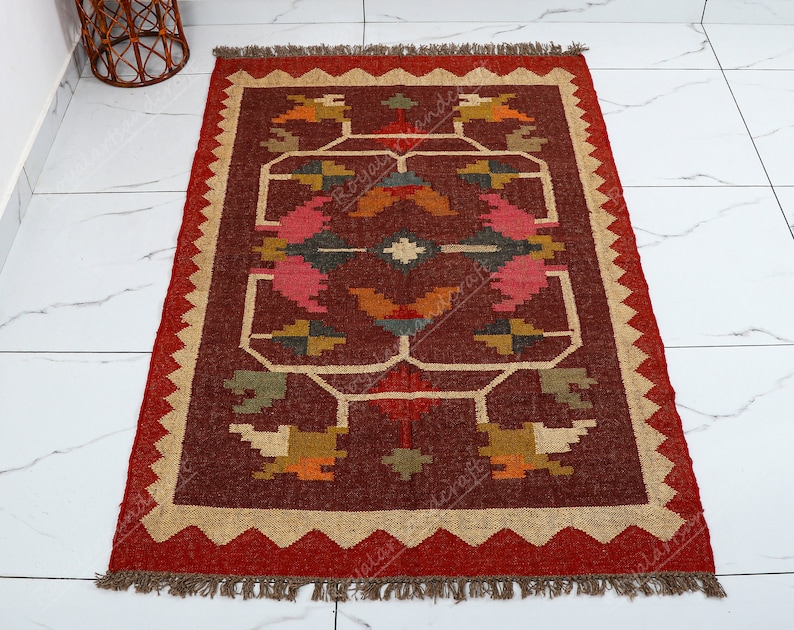 May include: A red, brown, and beige area rug with a geometric pattern. The rug has a fringe border.