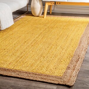 May include: A yellow jute rug with a natural jute border. The rug has a woven texture and is perfect for adding a touch of natural warmth to any room.