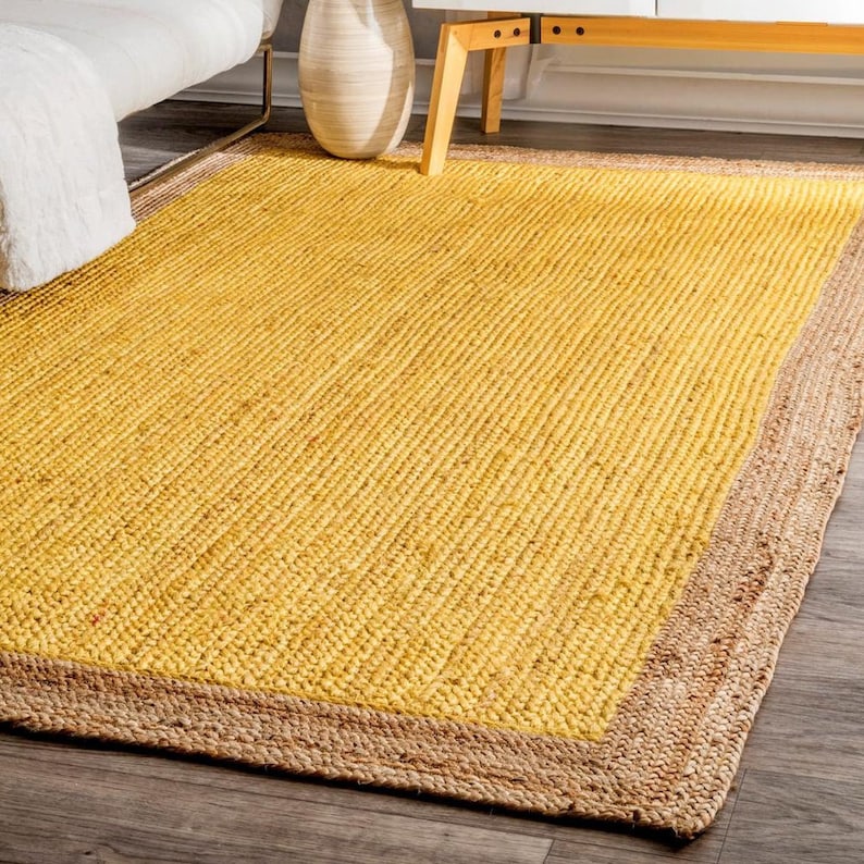 May include: A yellow jute rug with a natural jute border. The rug has a woven texture and is perfect for adding a touch of natural warmth to any room.