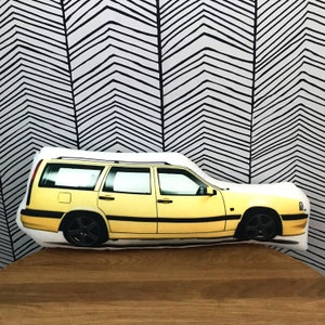 Pode incluir: Uma almofada de carro amarela com fundo branco. O carro é uma carrinha com um rack de teto preto e rodas pretas.