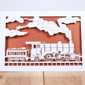 May include: White paper card with a cut-out design of a steam train with smoke and clouds. The train is labeled "MATTHEW".