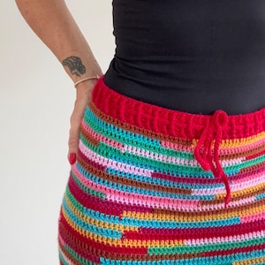 May include: A colorful crochet skirt with a red waistband and a drawstring. The skirt is made with a variety of colors, including pink, blue, green, and brown.