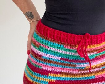 May include: A colorful crochet skirt with a red waistband and a drawstring. The skirt is made with a variety of colors, including pink, blue, green, and brown.