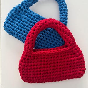 May include: Two crocheted bags, one red and one blue. The red bag is on top of the blue bag.