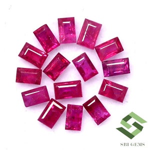May include: A collection of 13 rectangular ruby gemstones, each with a deep red hue and a polished finish. The gemstones are arranged in a circular pattern on a white surface.
