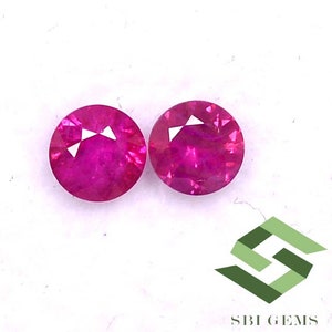 Peut inclure: Deux pierres précieuses rondes de couleur rose vif avec une taille facetée. Les pierres précieuses sont posées sur un fond blanc.