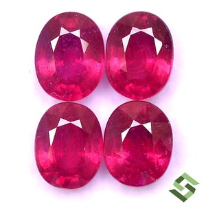 May include: Four oval-shaped ruby gemstones, each with a deep red color and a faceted cut. The gemstones are arranged in a square pattern on a white background.