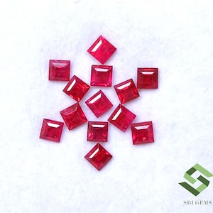 May include: A collection of eleven loose, vibrant red square-cut gemstones arranged in a cluster. Each stone features a faceted surface that reflects light, creating a brilliant appearance. The logo SBI GEMS is visible in the bottom right corner.