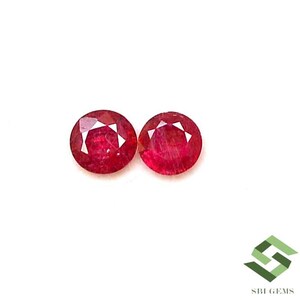 May include: Two round, red ruby gemstones with a faceted cut. The gemstones are set against a white background.