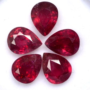Puede incluir: Cinco piedras preciosas de rubí en forma de pera, cada una con un color rojo intenso y un corte facetado, dispuestas en forma de flor.