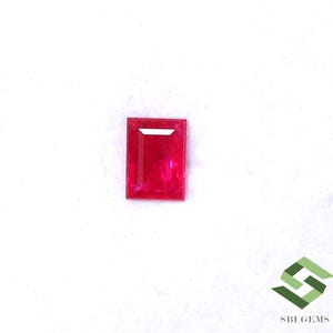 Könnte beinhalten: Ein rechteckiger, facettierter, leuchtend roter Edelstein mit einer weißen horizontalen Facette oben. Der Edelstein ist vor einem weißen Hintergrund platziert. Das Bild enthält auch das SBI GEMS-Logo in der unteren rechten Ecke.